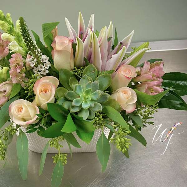 Mixed pink and cream flowers in a white rectangular vase with a succulent center