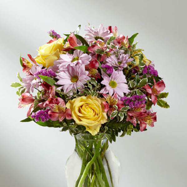 Mixed bouquet of yellow roses, pink daisies, and alstroemeria in a glass vase