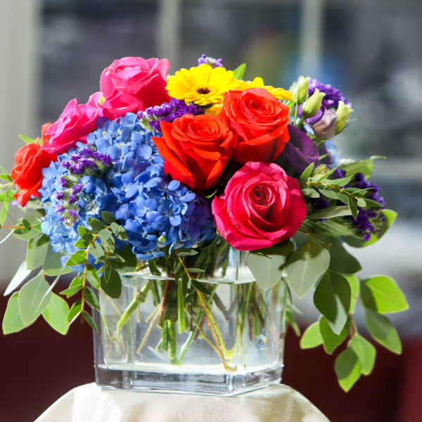 Colorful bouquet of roses, hydrangeas, and a yellow daisy in a glass vase