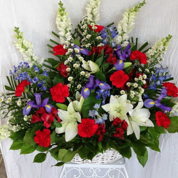 Large mixed flower arrangement in a white basket with red, white, and purple blooms