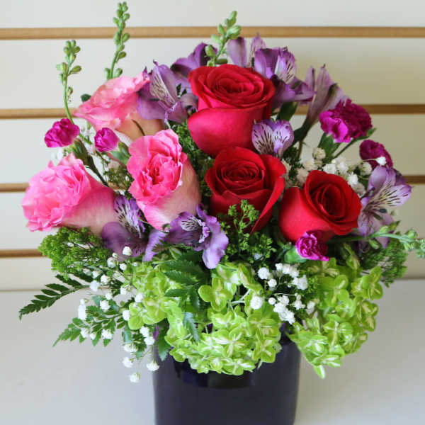 Bouquet of red and pink roses with purple flowers in a dark vase