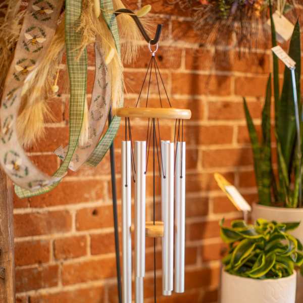 Silver wind chime hanging in front of a brick wall with potted plants nearby