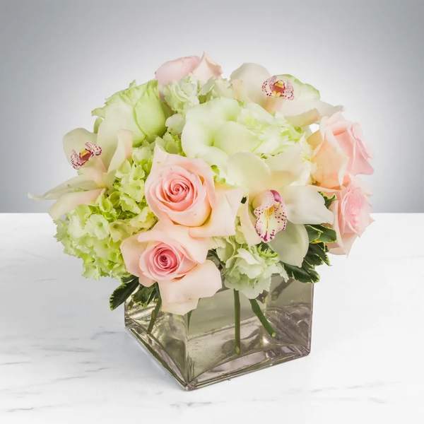 Pink roses and pale green-white flowers in a square glass vase