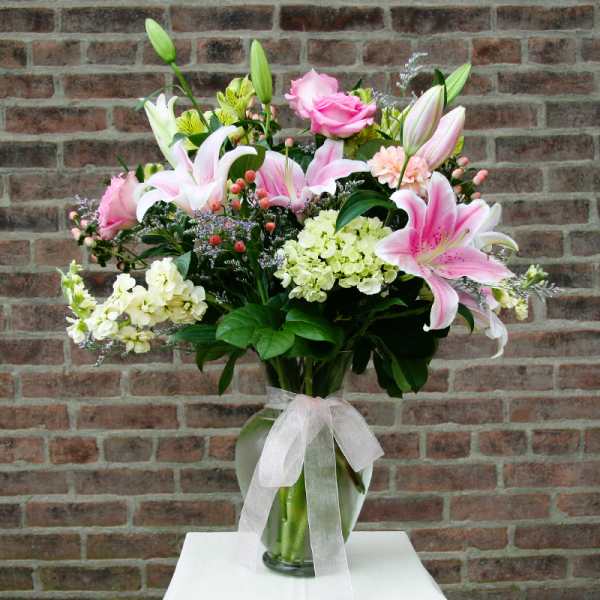 Pink lilies and roses arranged in a glass vase with a white ribbon