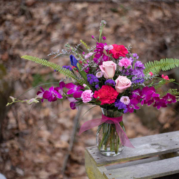 Mixed pink, purple, and red bouquet in a glass vase with a ribbon