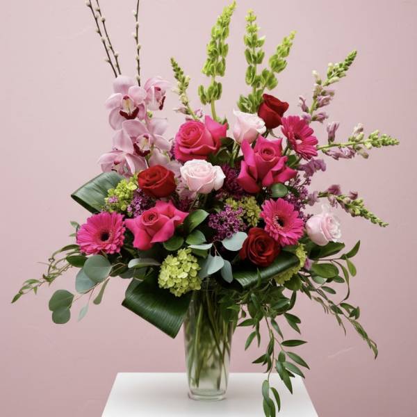 Tall vase arrangement of pink and red roses with gerbera daisies and orchids.