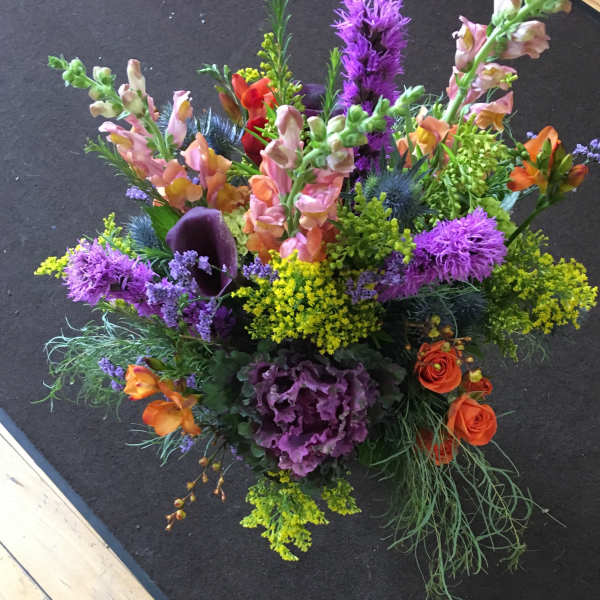 Tall mixed arrangement with purple, yellow, and orange flowers including snapdragons and roses