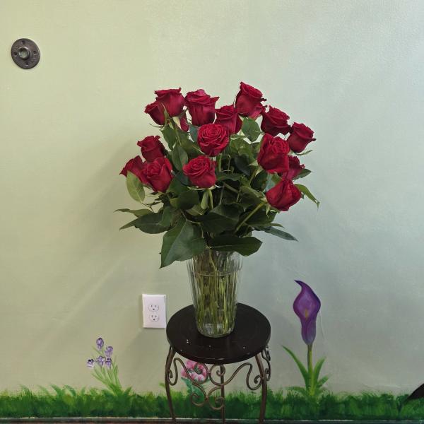 Red roses arranged in a clear glass vase on a small stand