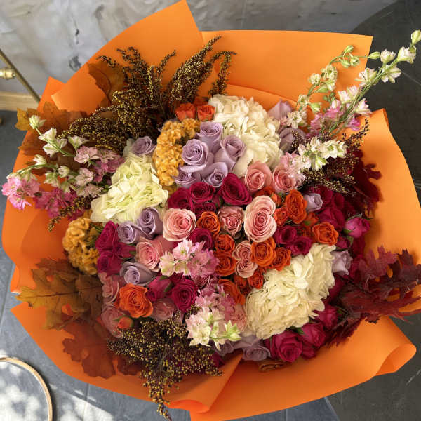 Mixed bouquet of roses and hydrangeas wrapped in bright orange paper