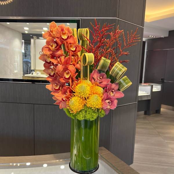 Orange and pink orchids with yellow blooms in a tall green vase