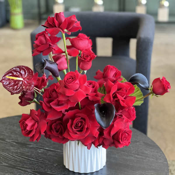 Red rose arrangement with dark calla lilies in a white vase