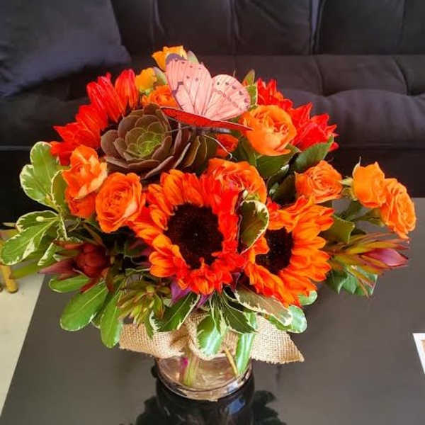 Bright orange sunflower and rose arrangement with succulent in a glass vase
