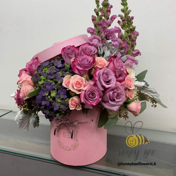 Pink and lavender roses in a pink hatbox with purple blooms
