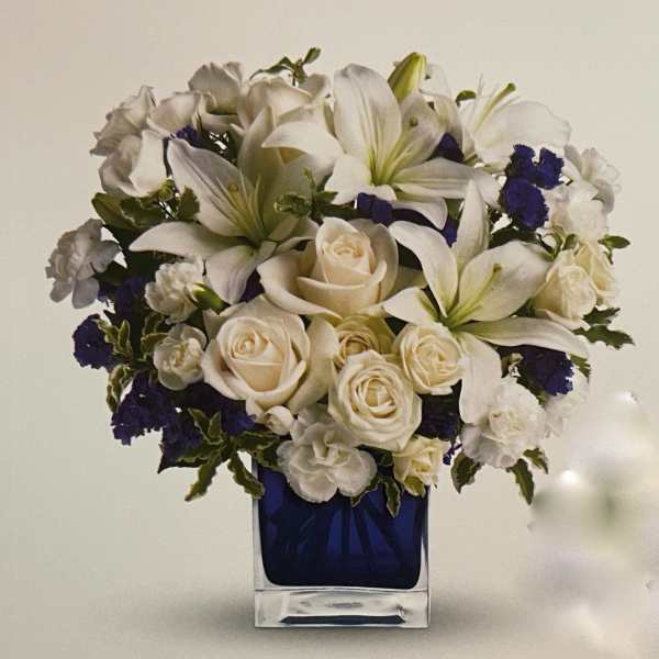 White lilies and roses in a blue glass vase with dark blue accents