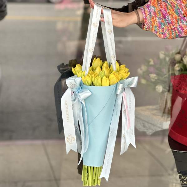 Yellow tulip bouquet wrapped in light blue paper with ribbon handles