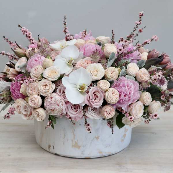 Low pink and white arrangement of roses, peonies, and orchids in a round white ceramic vase