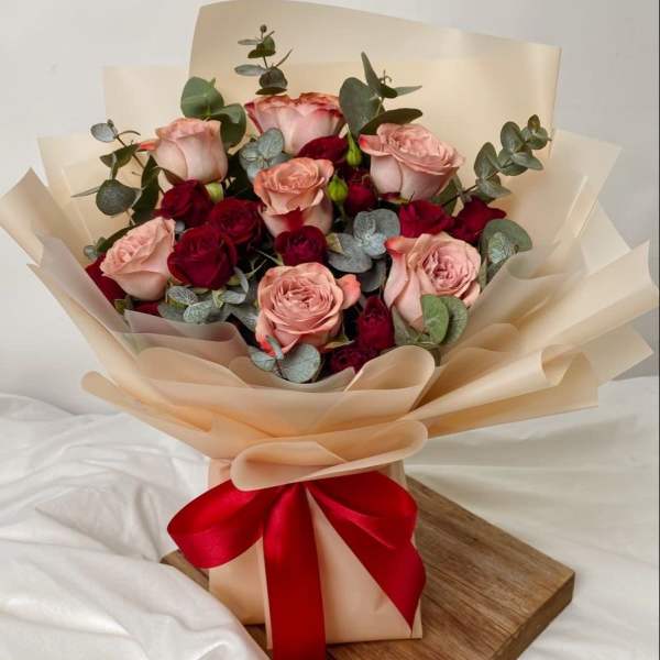 Bouquet of pink and red roses wrapped in beige paper with a red ribbon
