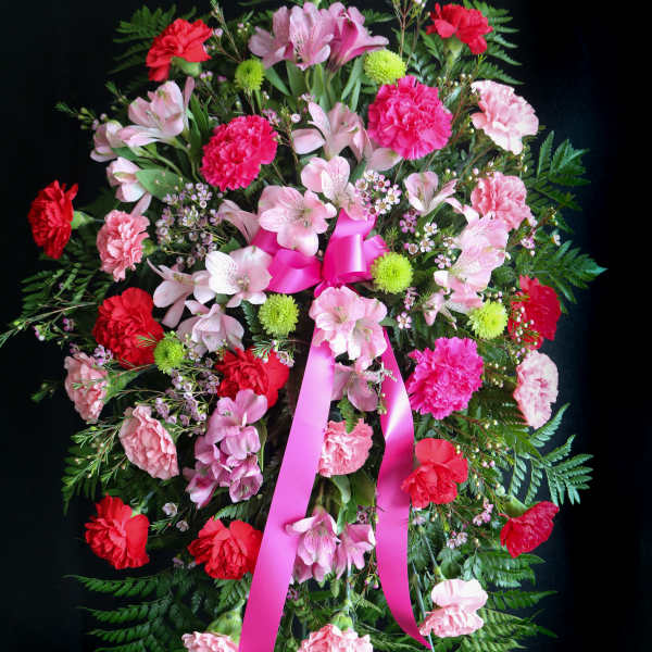 Standing floral wreath with pink and red carnations and a pink ribbon