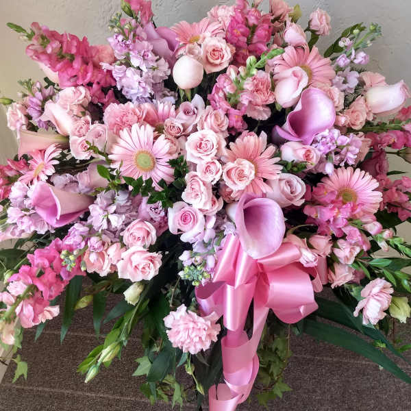 Large pink floral spray with roses, gerbera daisies, calla lilies, and a ribbon bow