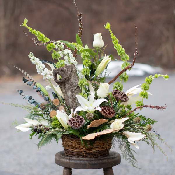 White lilies and roses in a wicker basket with branches and seed pods