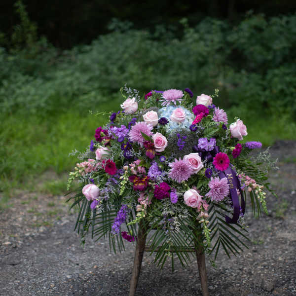 Standing floral spray with pink and purple blooms on a wooden easel