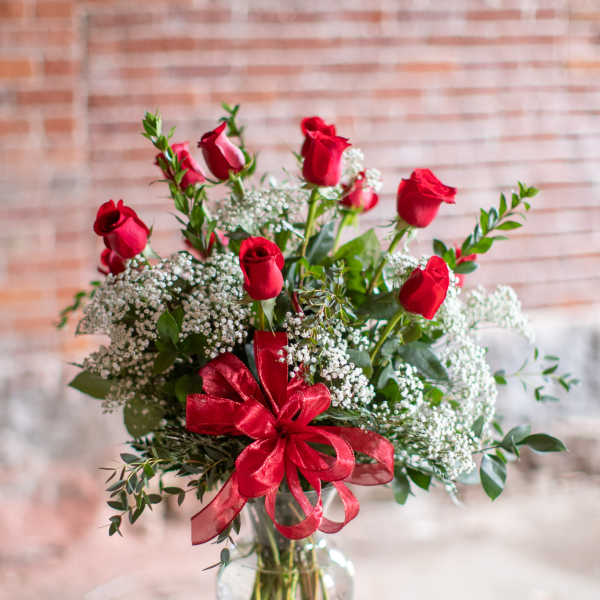 Red roses and baby's breath in a clear glass vase with a red ribbon