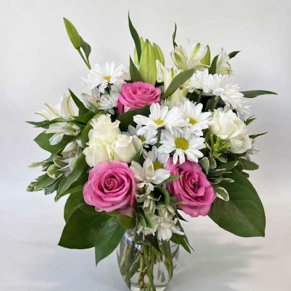 Bouquet of pink roses, white daisies, and white roses in a clear glass vase