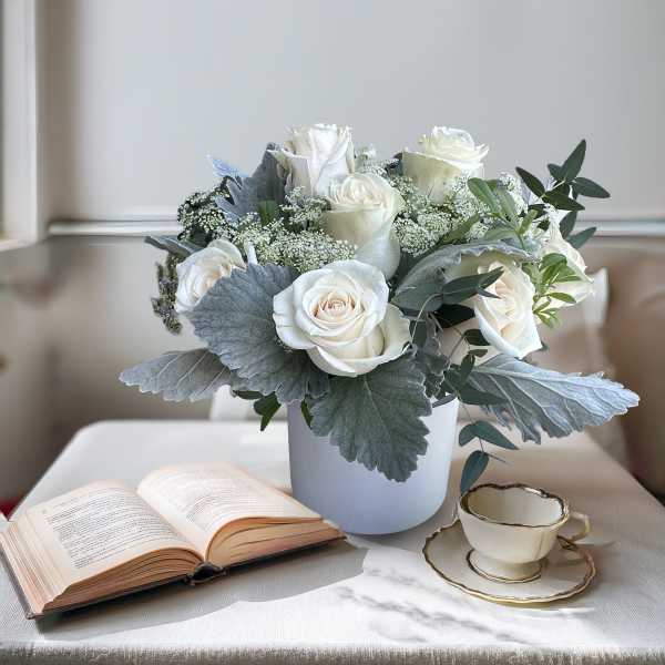 White roses in a pale blue vase with silver foliage