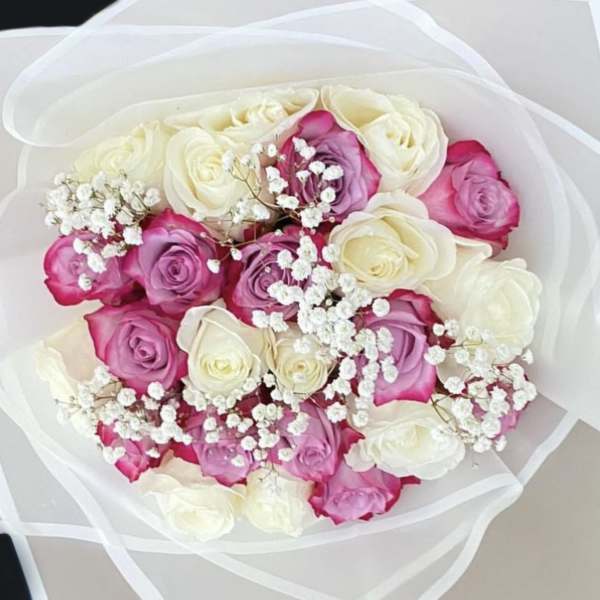 Bouquet of white and pink roses with small white filler flowers wrapped in sheer white paper