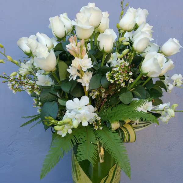 White roses and orchids arranged in a green glass vase