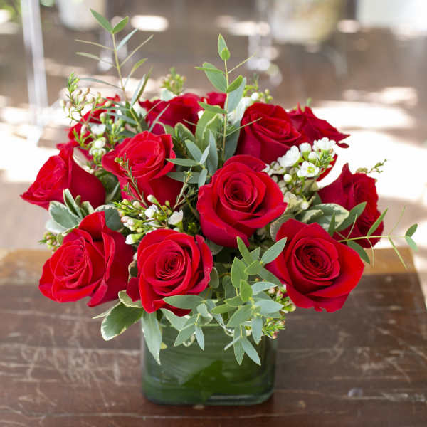 Red roses arranged in a square glass vase with white filler flowers
