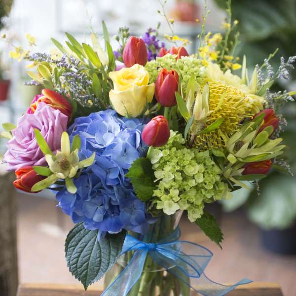 Colorful bouquet of mixed flowers in a glass vase with a blue ribbon