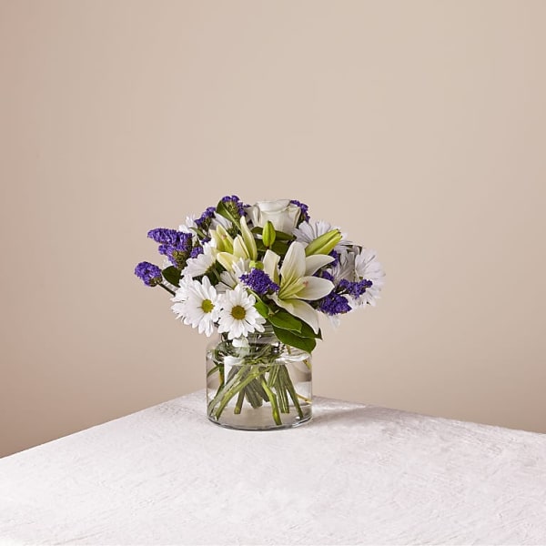White lilies and daisies in a clear glass vase with purple filler flowers