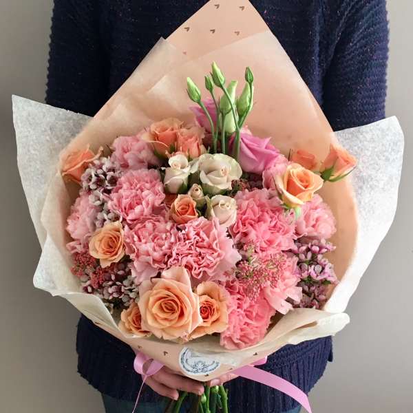Handheld bouquet of pink and peach roses with carnations wrapped in paper
