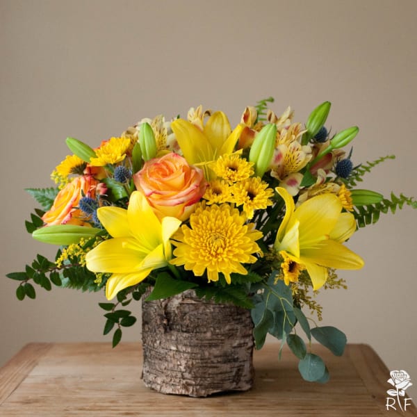 Yellow lilies and roses arranged in a birch bark container