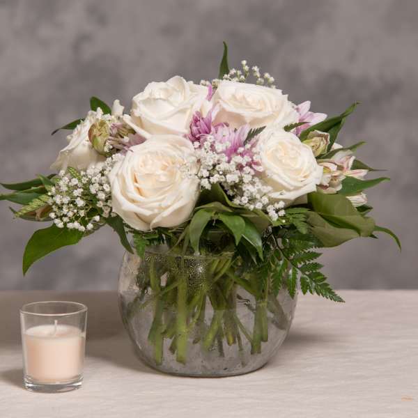 White rose bouquet in a glass vase with a small candle beside it