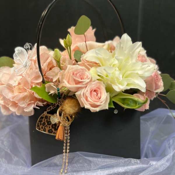 Pink and white floral arrangement in a black handbag-shaped container