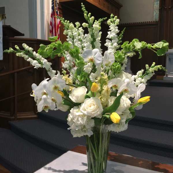 White flowers and yellow tulips arranged in a clear glass vase