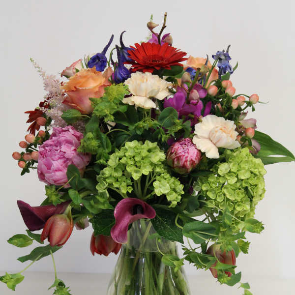 Mixed bouquet of pink, peach, red, purple, and green flowers in a clear glass vase