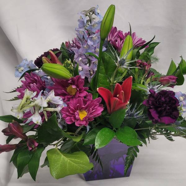 Mixed bouquet with lilies, daisies, and purple flowers in a purple vase