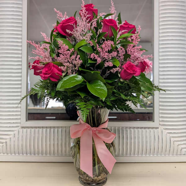 Tall arrangement of hot pink roses with pink filler in a clear glass vase tied with a pink bow.