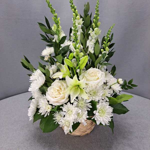 White floral arrangement in a wicker basket with lilies and roses