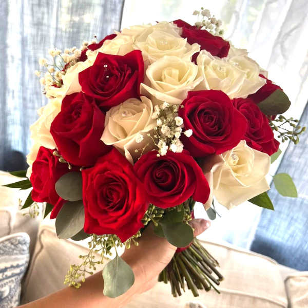 Handheld bouquet of red and white roses with small white filler flowers