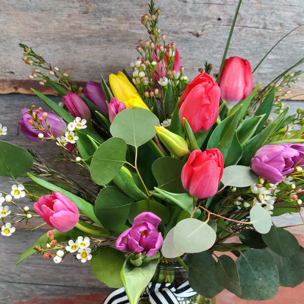 Colorful tulip bouquet in a glass jar with a striped ribbon