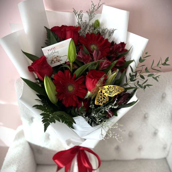 Red roses and gerbera daisies in white wrap with a birthday card