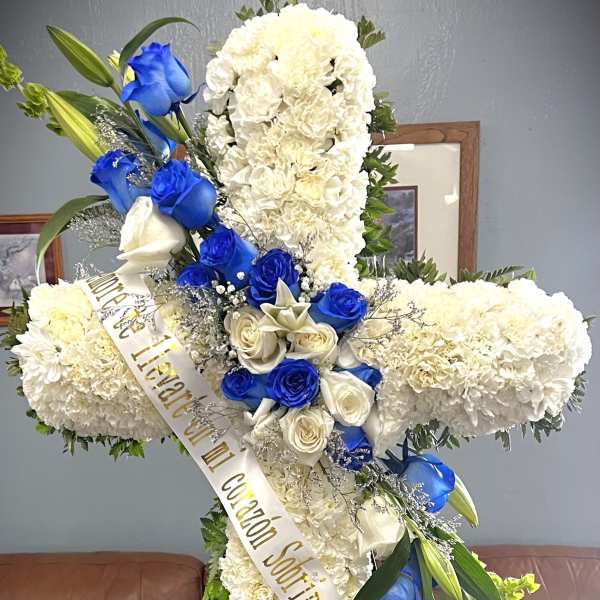 White floral funeral cross with blue and white roses and a memorial ribbon