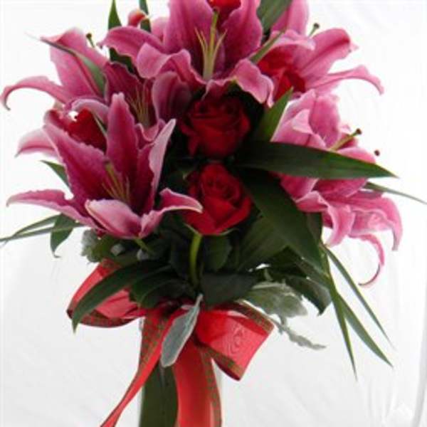 Pink lilies and red roses in a tall glass vase with a red ribbon