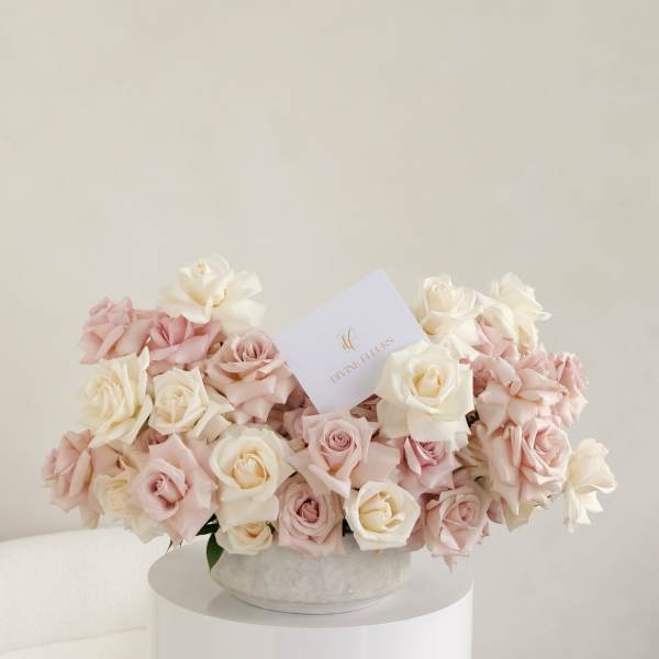 Blush and ivory roses arranged in a round hatbox with a card.