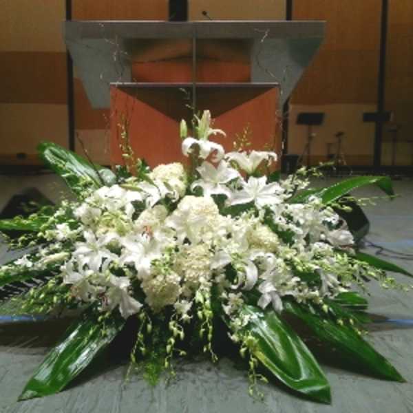 Large white lily and mum arrangement displayed in front of a wooden podium