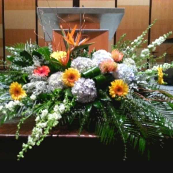Large low centerpiece of hydrangeas, gerbera daisies, and a tropical bloom in front of a podium